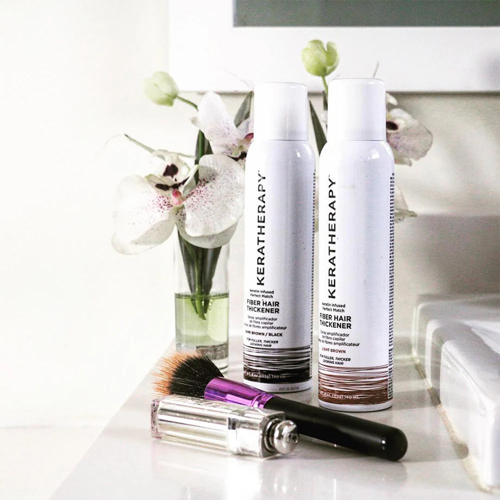 Two bottles of Keratherapy hair product on a white surface with flowers in the background.