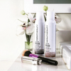 Two bottles of Keratherapy hair product on a white surface with flowers in the background.